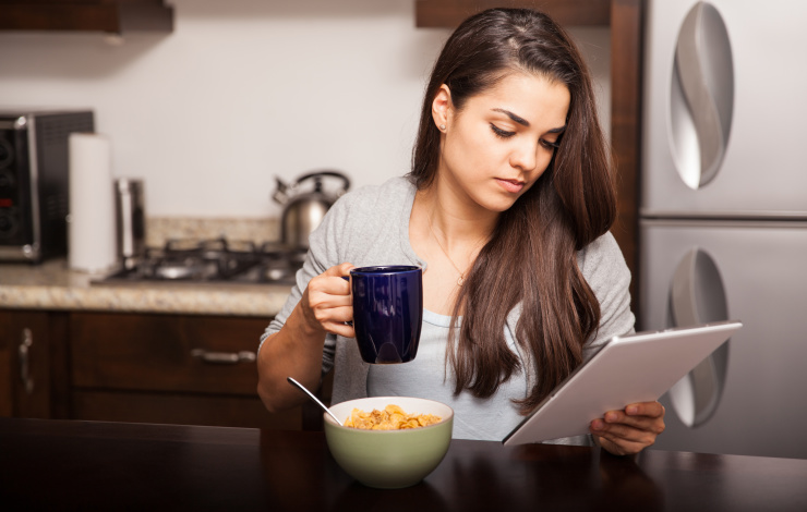 Young woman using a tablet computer to read the news and some emails while having breakfast at home