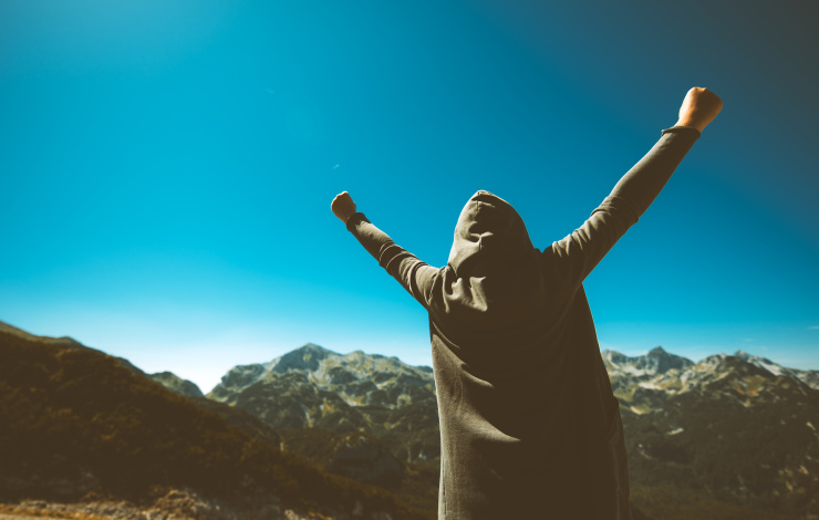 Victorious female person standing on mountain top with arms raised in V. Winning and success. Achievement and accomplishment in life. Toned image.