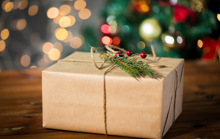present wrapped in simple brown paper with lit tree in the background
