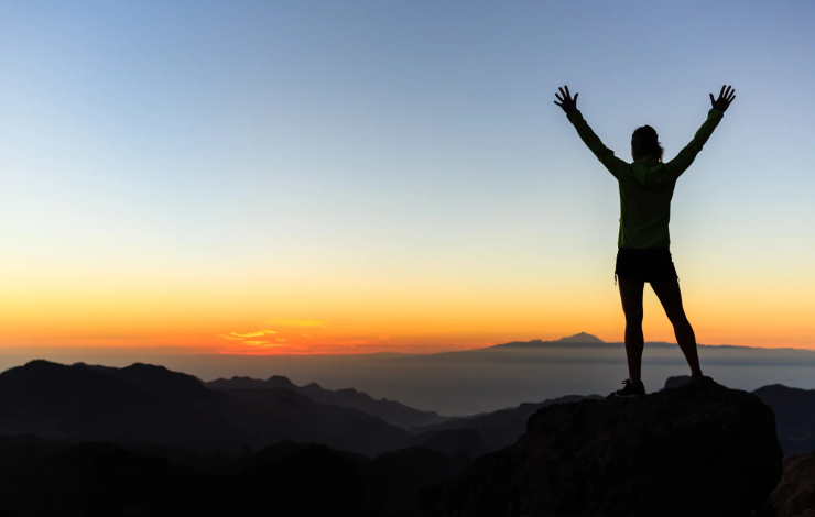 person on top of mountain achieving goals