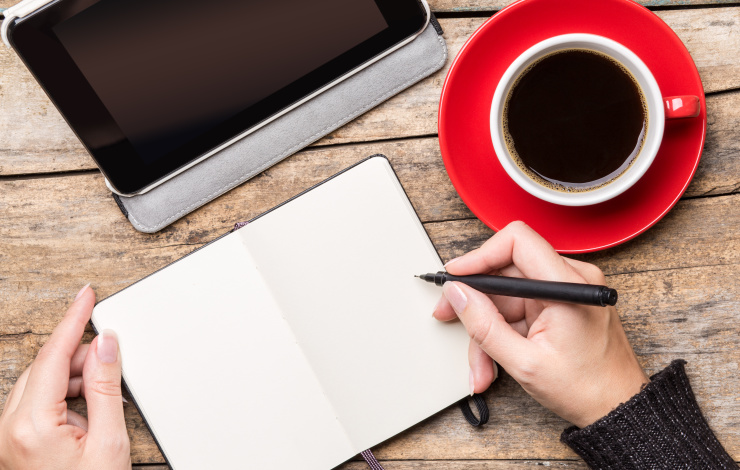 woman writing in notebook with tablet and coffee