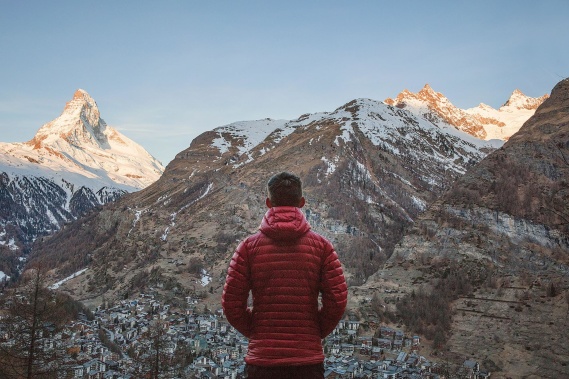 man in red jacket facing a mountain