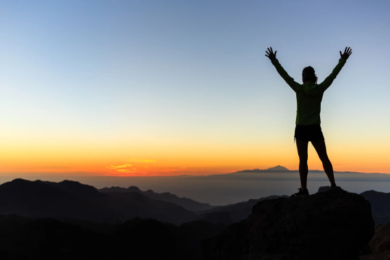 person on top of mountain achieving goals
