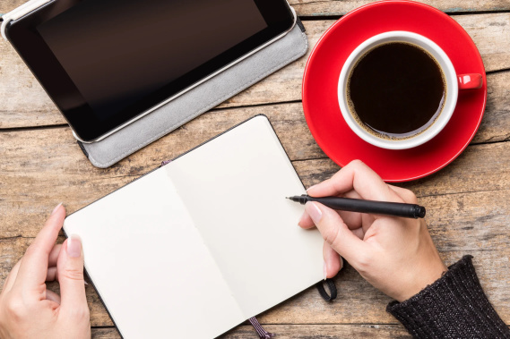 woman writing in notebook with tablet and coffee