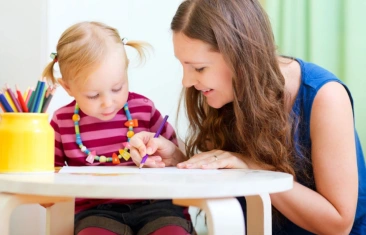 Picture of a woman helping a child color on a piece of paper.