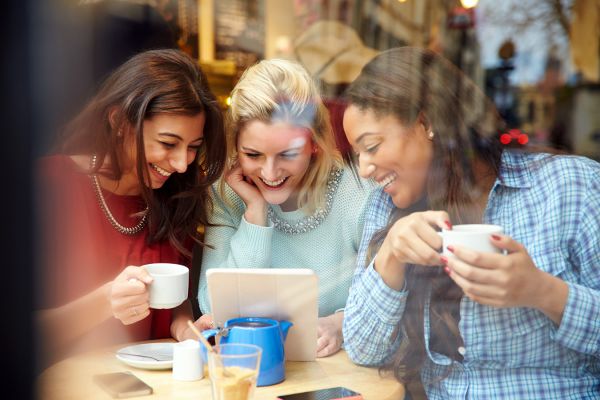 Three women huddled together looking at tablet in coffee shop