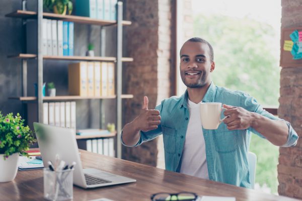 Guy giving a thumbs up while drinking coffee and working on laptop