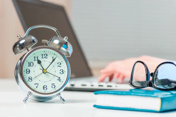 Person working on laptop with a focus on the desk clock