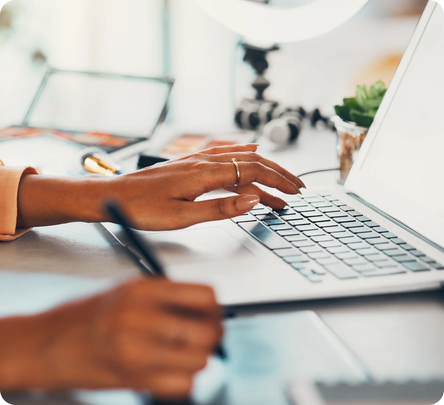 Close-up of entrepreneur typing on laptop while taking notes at desk with creative workspace tools nearby