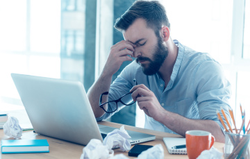 frustrated man at his computer rubbing the bridge of his nose