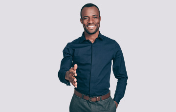 Handsome young African man stretching out hand for shaking and smiling to you while standing against grey background