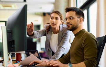 A woman pointing out something on a computer monitor to a coworker
