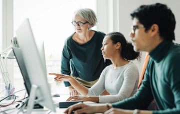 Two women and a man looking at something on a computer monitor