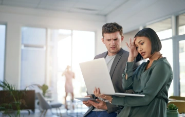 A man and woman looking perplexed while looking at a laptop screen