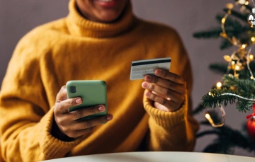 Woman smiling holding her phone in one hand and a bank card in the other