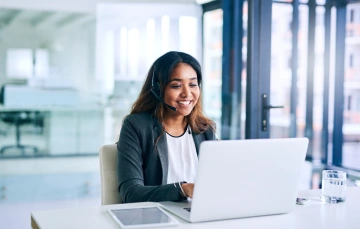 A smiling woman wearing a headset and typing on her laptop