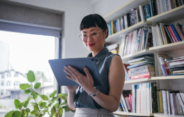 A woman in glasses staring down at an iPad in her hand
