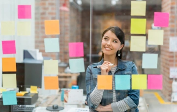 Woman standing in front of a board of different color sticky notes