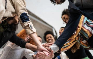 A group of people gathered together with their arms in the center, symbolizing teamwork and collaboration.