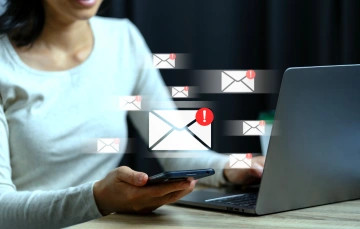 A woman using a laptop and smartphone with floating email icons showing unread message alerts.