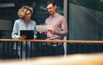 Two business professionals reviewing CRM reports together using a tablet and printed documents