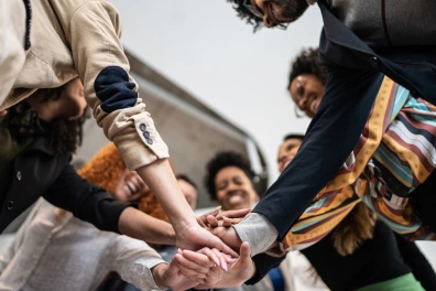 A group of people gathered together with their arms in the center, symbolizing teamwork and collaboration.