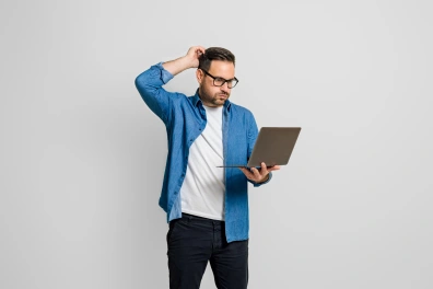 A man looking at his laptop scratching his head and while looking slightly frustrated