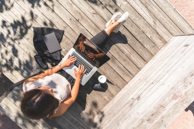 A woman sitting on a wooden deck outdoors working on a laptop
