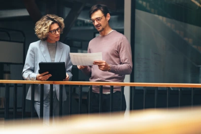 Two business professionals reviewing CRM reports together using a tablet and printed documents