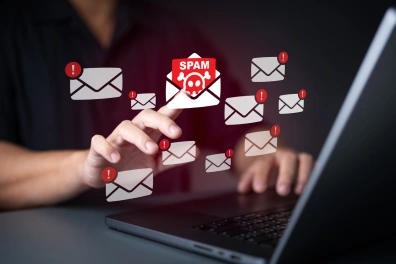 Illustration of a person’s hand interacting with a laptop as numerous email icons with red alert symbols float above it, with one envelope labeled “SPAM” featuring a skull—suggesting issues with email deliverability or performance.
