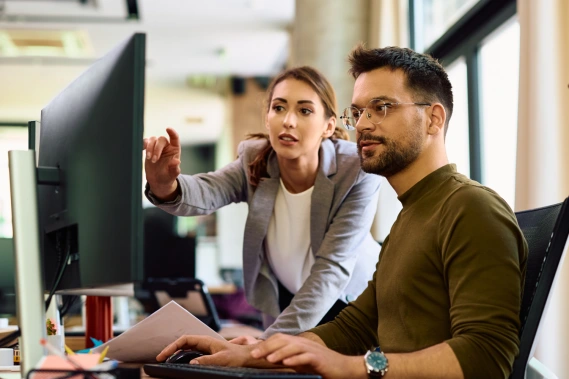 A woman pointing out something on a computer monitor to a coworker