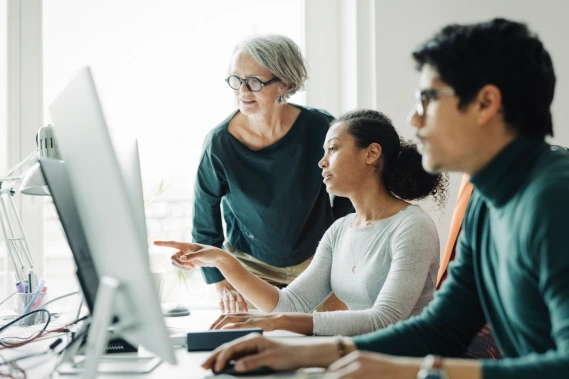 Two women and a man looking at something on a computer monitor