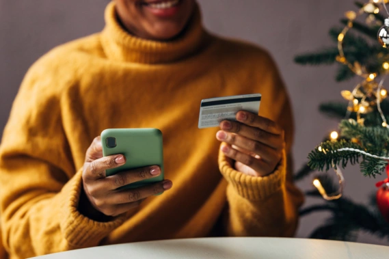Woman smiling holding her phone in one hand and a bank card in the other