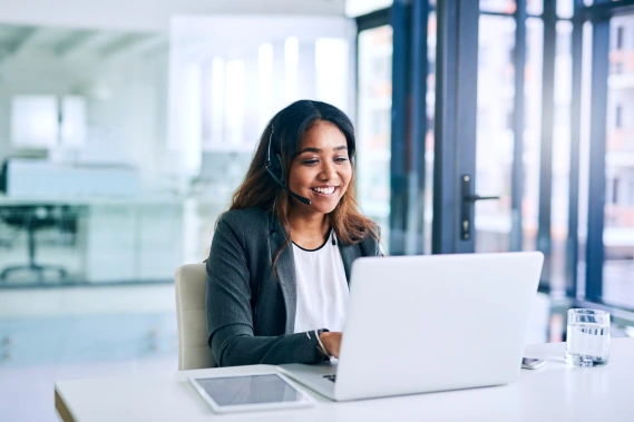 A smiling woman wearing a headset and typing on her laptop