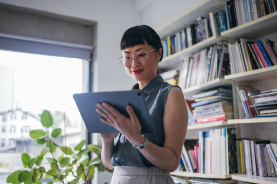A woman in glasses staring down at an iPad in her hand