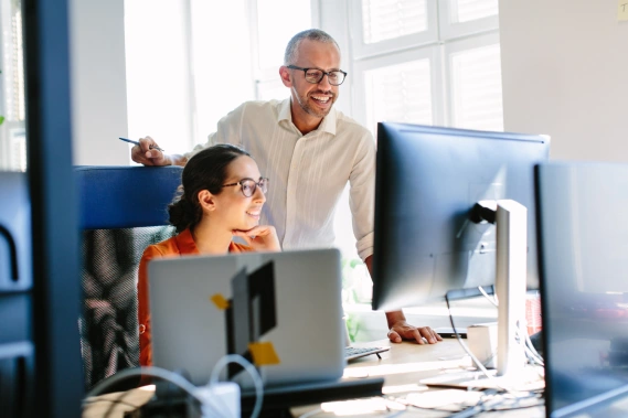 A man and woman smiling while looking at a computer monitor