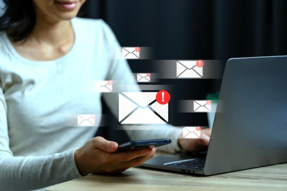 A woman using a laptop and smartphone with floating email icons showing unread message alerts.