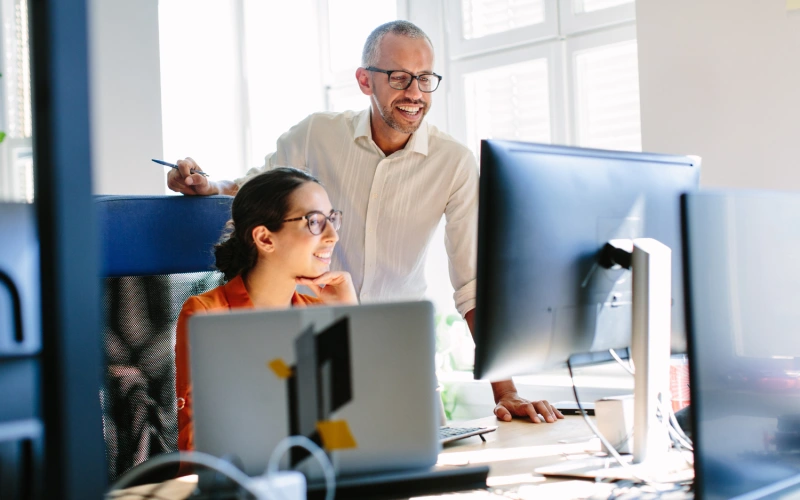 A man and woman smiling while looking at a computer monitor